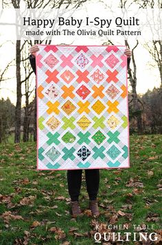 a woman holding up a colorful quilt in front of her face and trees with leaves on the ground