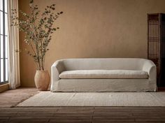 a white couch sitting in front of a window next to a vase filled with flowers