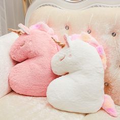 two stuffed unicorns are sitting on a couch with pink and white pillows in front of them