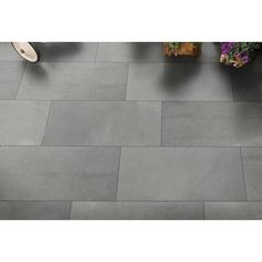 a tile floor with grey tiles on the bottom and one in the middle, surrounded by potted plants