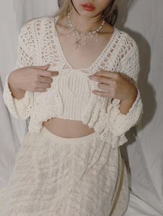 a woman wearing a white lacy top and skirt with her hands on her hips, posing for the camera