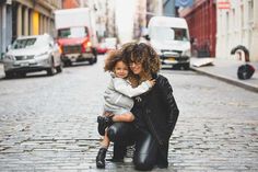 a woman holding a child in her arms while standing on a cobblestone street