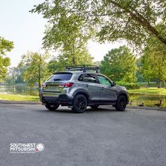 a gray suv parked on the side of a road next to a lake and trees