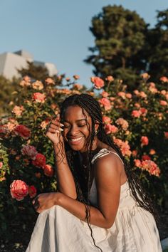 a woman sitting on the ground in front of some flowers and talking on her cell phone