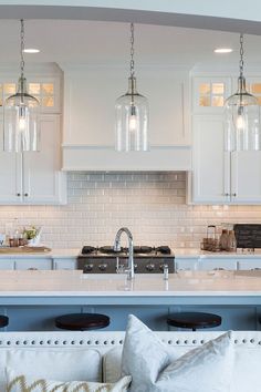 a kitchen with white cabinets and an island in front of the counter top is lit by three pendant lights