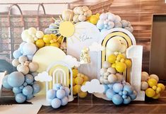 an arch made out of balloons and other items is displayed on a wooden table in front of a wall