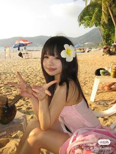 a young woman sitting on top of a sandy beach next to a palm tree and holding a coconut