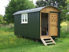 a small green shed with steps leading up to the door and windows on it's side