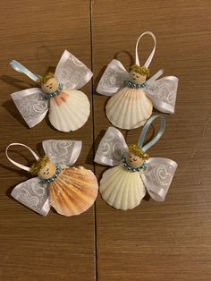 three seashells with angel wings and bows are on a wooden table, next to each other