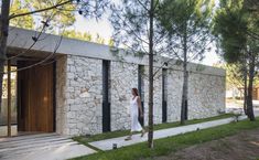 a woman walking past a stone building next to trees