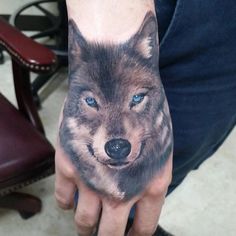 a man's hand with a wolf tattoo on it and blue eyes in the middle