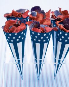 four blue and white striped vases with red flowers in them on a wooden table