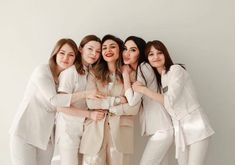 four women in white posing for the camera with their arms around each other and smiling