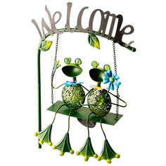 a metal welcome sign with two frogs on it's back and the word welcome above them