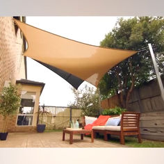 an outdoor area with a couch, table and large shade sail on the side of a house