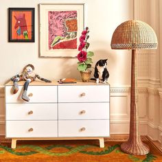 a white dresser sitting next to a lamp on top of a hard wood floor covered in furniture