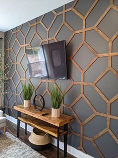 a tv mounted to the side of a wall next to a wooden table with two potted plants on it