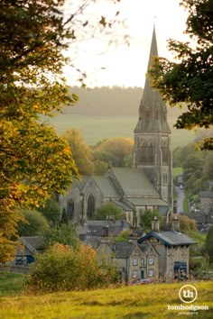 an old church sits in the middle of a town surrounded by trees and grass, with autumn foliage on the ground