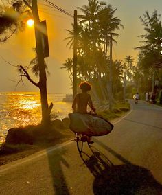 a person riding a bike with a surfboard strapped to the handlebars as the sun sets