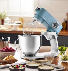 an electric mixer on a kitchen counter with fruit and other food items in the background