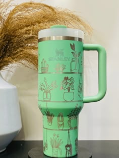 a green travel mug sitting on top of a black table next to a potted plant