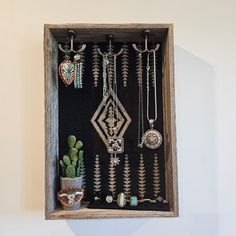 a wooden box with various necklaces hanging from it's sides and a cactus in the middle