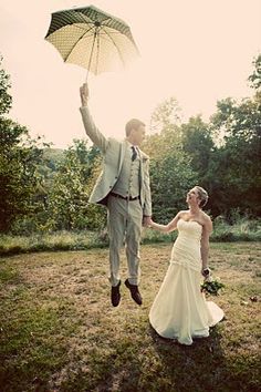 a bride and groom jumping in the air with an umbrella over their heads as they hold hands