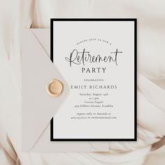 a white and black retirement party card with a gold button on the front, sitting on top of an envelope