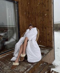 a woman is sitting in a chair on the porch covered with blankets and she's sleeping