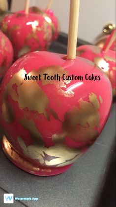 some pink and gold apples with wooden sticks sticking out of them on top of a counter