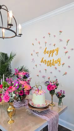 a birthday cake on a table with pink flowers and greenery in front of it