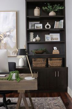 a desk with a laptop on top of it next to a book shelf and vases