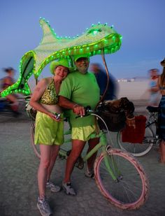 two people standing next to each other near a bike with a green fish on it