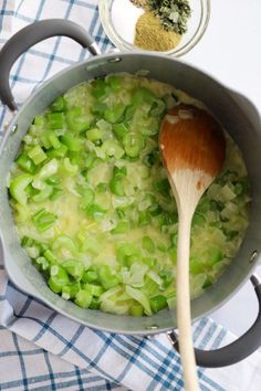 a wooden spoon in a pot filled with green onions and seasoning next to a jar of spices