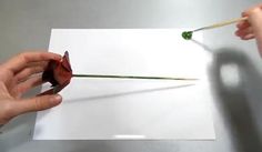 two hands are holding a piece of paper with a flower on it and one hand is holding a pencil