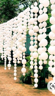 there are many white balls hanging from the ceiling in this garden area that is lined with potted plants and trees