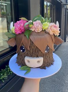 a cake shaped like a cow with flowers on it's head is being held by a hand