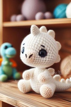 a crocheted white cat sitting on top of a wooden shelf next to other stuffed animals