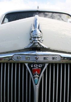 the front end of an old white car with chrome grills and emblem on it