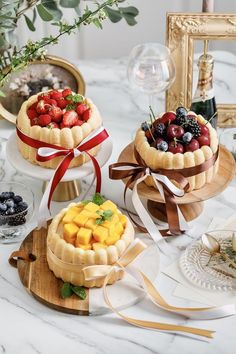 there are three cakes on the table and one is decorated with berries, pineapples, blueberries, raspberries