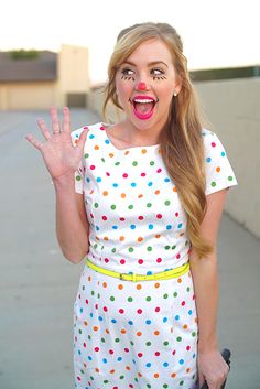 a woman in polka dot dress making a funny face with her hand and holding a suitcase