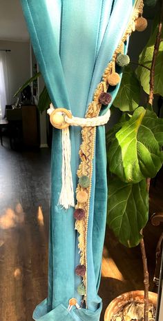 a blue curtain with tassels hanging from it's side in front of a potted plant