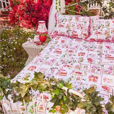 a bed covered in pink flowers next to a white fence and red flowers on the ground