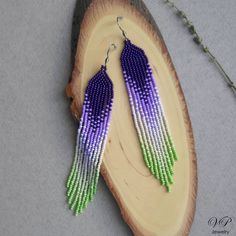 purple and green seed beaded earrings sitting on top of a piece of wood