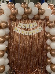 a gold and white balloon arch with happy birthday banner on the top, surrounded by balloons