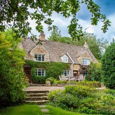 a stone house surrounded by lush green trees and flowers in the foreground, with steps leading up to it