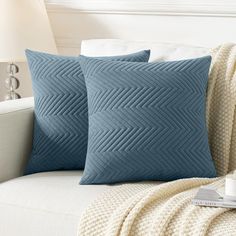 two blue pillows sitting on top of a couch next to a white blanket and lamp