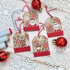 four christmas tags with santa and reindeer on them, next to some holiday decorations in front of snowflakes