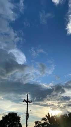 the sun is setting behind some clouds in the blue sky with power lines and palm trees