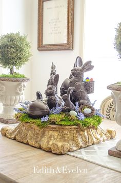 the table is decorated with statues of rabbits and eggs in an egg basket on top of moss